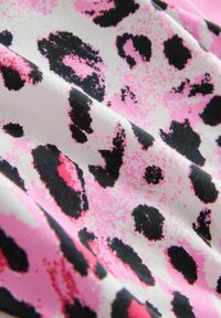 Leopardmönstrad tyg med en vit bakgrund och svarta och rosa fläckar, slät textur och djärv färgkontrast.