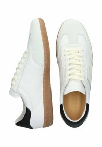 Valkoiset tennarit, joissa on nahkainen päällinen, samettivaatteet ja kuminen pohja. Varustettu mustalla kantatunnuksella ja litteillä nauhoilla.