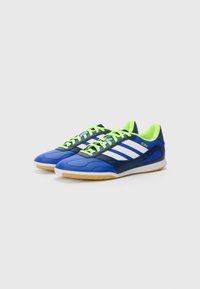 Blauwe en marineblauwe sportschoenen met witte strepen en neon groene veters. Heeft een gestructureerde bovenkant en rubberen zool. Lichtgewicht ontwerp.