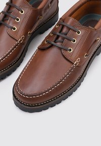 Zapatos de cuero marrón con un acabado suave, costuras contrastantes, punta redonda y suelas de goma negra. Presentan ojales dorados y un diseño de cordones.