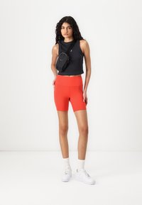 Black cropped tank top, red high-waisted bike shorts, white sneakers, and a small black crossbody bag. Smooth fabric with a fitted design.