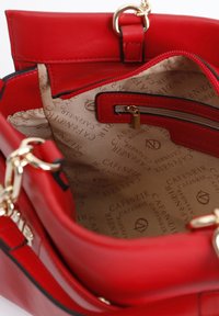 Interno di una borsa a tracolla in pelle rossa con una fodera beige a motivo. Presenta una tasca con zip e dettagli in oro.