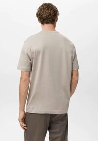 Beige bomulds-T-shirt med afslappet pasform, korte ærmer og lige kant. Ingen synlige mønstre eller pynt. Set bagfra.