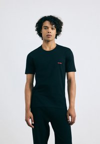 T-shirt en coton noir avec un design ajusté, un col rond, des manches courtes et un petit logo "HUGO" rouge sur la poitrine.