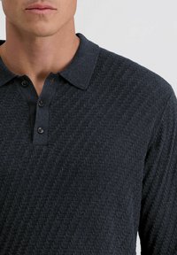 Donkerblauwe poloshirt met een gestructureerd, diagonaal patroon. Met kraagontwerp en twee knopen aan de hals. Gladde stoftextuur.