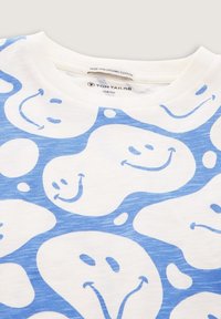 Weißes T-Shirt aus biologischer Baumwolle mit einem blauen Muster von lächelnden Gesichtern in verschiedenen Formen, mit Rundhalsausschnitt und weicher Textur.