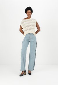 Krēmveida adīta blūze ar vaļīgu adījumu, kombinēta ar augstām gaismām zilām džinsiem, kuros ir sānu pogas. Vilkta ar melniem augstpapēžu apaviem.