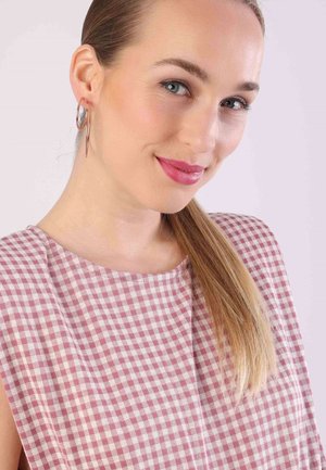 Rozenpatroon, mouwloos topje met een ronde halslijn en een geruite ontwerp in roze en wit. Het model draagt grote ringoorbellen en heeft lang haar.