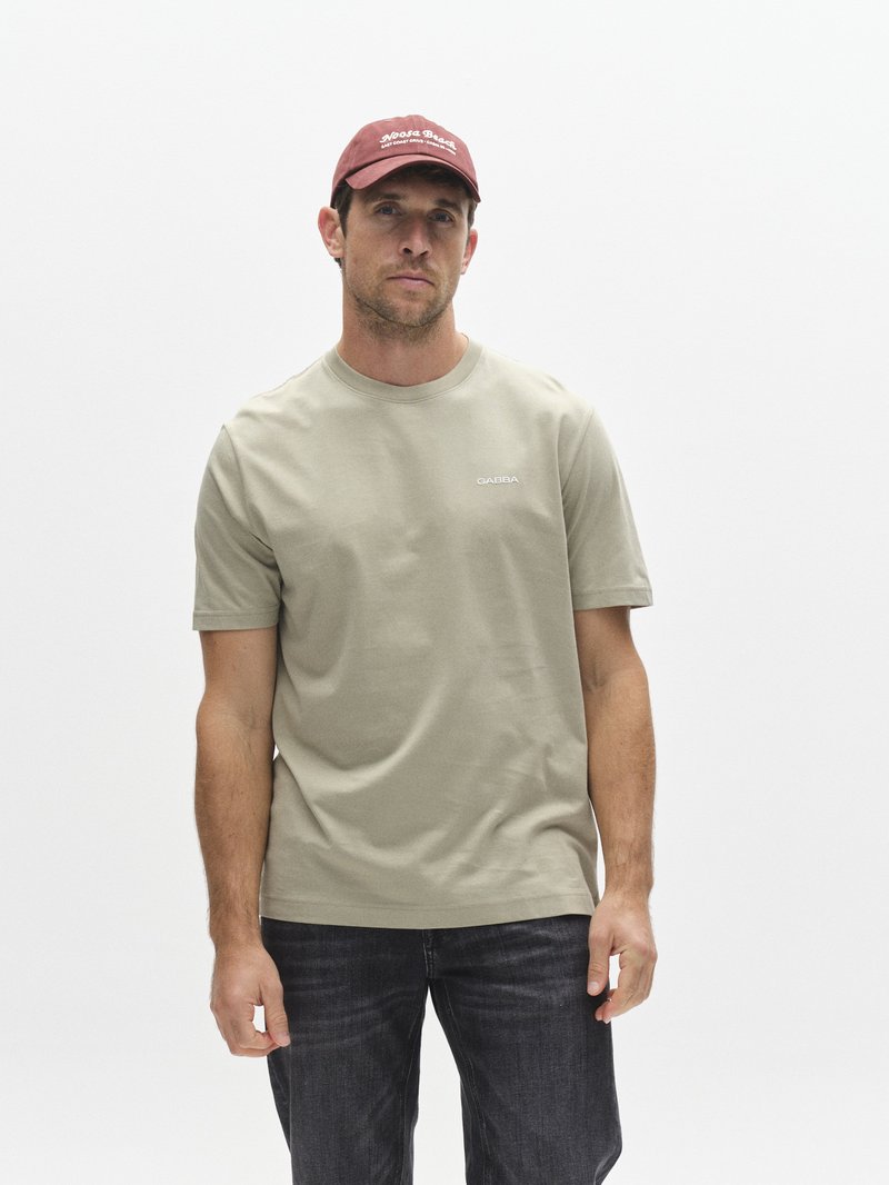 Olivgrön bomulls-t-shirt med korta ärmar och rund halsringning, kombinerad med mörka jeans och en vinröd keps med vit text.