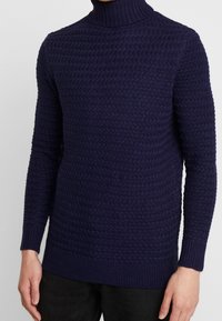 Granatowy sweter z golfem wykonany z dzianiny, z teksturowanym, wypukłym wzorem i długimi rękawami, z prążkowanymi mankietami i dołem, co zapewnia dopasowany wygląd.