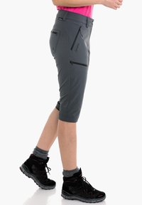 Pantalones cortos grises hasta la rodilla, hechos de una tela ligera, con bolsillos con cremallera y una cintura ajustada. Combinados con zapatos de senderismo negros.