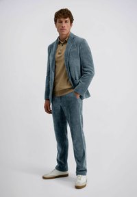 Lichtblauw corduroy kostuum met verticale strepen, gecombineerd met een tan polo. Gestyled met witte sneakers en een ontspannen pasvorm, met een notch lapel.