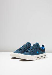 Modré sportovní boty s hladkou texturou, zdobené tmavě modrou hvězdou, jasně modrými tkaničkami a bílou gumovou podrážkou.