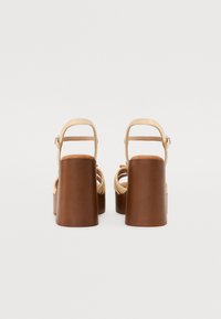 Brune høyhælte sandaler med en kraftig hæl og en beige stropp. Åpen tå-design med en jevn tekstur og justerbar ankelstropp.