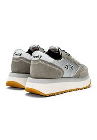 Zapatillas de ante gris con acentos blancos, un talón texturizado y una suela blanca gruesa. Presentan un logo y un diseño triangular en los laterales.