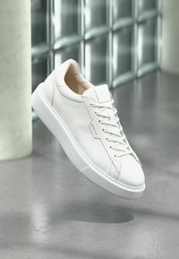 White leather sneakers with a rounded toe, lace-up design, and subtle branding. Features a smooth texture and a contrasting white rubber sole.