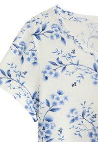 Kortærmet top i cremefarvet stof med en blå blomsterprint og blade, blød tekstur og rund halsudskæring.