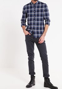 Granatowa i jasnoniebieska koszula w kratę z długimi rękawami, zestawiona z ciemnoszarymi spodniami typu slim fit i czarnymi butami sznurowanymi.