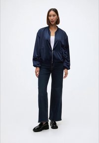 Jūras spēku satīna bomber jakas ar ribotu apkakli un piedurknēm, apvienota ar tumši ziliem platām biksem un melniem platformas apaviem. Zem tās baltā blūze.