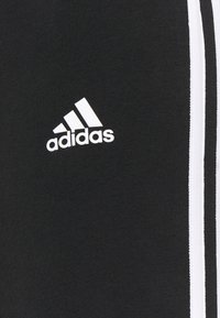 Zwarte sportbroeken gemaakt van gladde stof, met witte zijstrepen en een klein wit Adidas-logo aan de voorkant.