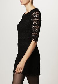 Robe mini en dentelle noire avec des manches trois-quarts, mettant en avant des motifs floraux complexes et une silhouette ajustée, texture lisse, ourlet à volants.