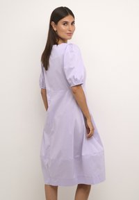 Palu šviesiai levandų spalvos suknelė su pūstomis rankovėmis, turinti laisvą siluetą ir kelių ilgio hemą. Pagaminta iš lygaus audinio, su švariomis linijomis ir minimaliais akcentais.