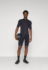 Conjunto de ciclismo negro que incluye una camiseta de manga corta con cremallera frontal y pantalones cortos acolchados. Acompañado de un casco y zapatos negros.