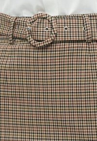 Ζώνη με καρό σχέδιο και στρογγυλή αγκράφα, σε αποχρώσεις καφέ, πράσινου και κρέμ, με υφασμάτινη υφή και ασημένιες μεταλλικές λεπτομέρειες.