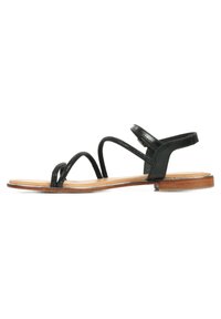 Sandali neri in pelle con cinturini sottili, suola piatta e chiusura con fibbia alla caviglia. Texture liscia con un design minimalista.