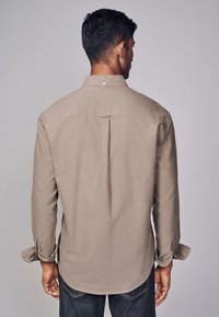 Lange mouwen, lichtbruine blouse met een rugplooien, afgeronde zoom, knoopmanchetten en een enkele knoop bij de kraag, gemaakt van gestructureerde stof.