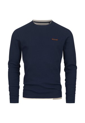 Meriino sininen ribbattu pitkähihaine neule, jossa on pyöreä kaula-aukko ja ruskea yksityiskohta vasemmassa rinnassa. Pehmeä rakenne ja kapea malli.