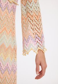 Manche de robe en dentelle présentant un motif zigzag multicolore dans des teintes pastel d'orange, de vert, de violet et de rose, avec des bords festonnés.
