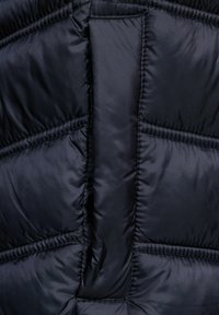 Mörkblå puffjacka i tyg med en slät, glänsande yta, med diagonala sömmar och vadderade sektioner för isolering.