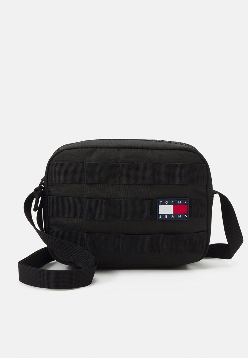 Borsa a tracolla rettangolare nera realizzata in tessuto resistente, con una patch del logo Tommy Jeans e accenti in tessuto a nastro. Include una tracolla regolabile.