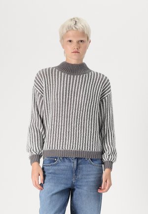 Grijs en wit gestreepte gebreide trui met een hoge hals, oversized pasvorm en ribgebreide manchetten en zoom, gedragen met blauwe denim jeans.