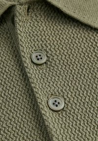 Gros plan sur un tissu tricoté vert texturé avec deux boutons ronds gris-vert à quatre trous, cousus en rangée verticale.