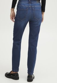 Tmavě modré skinny džíny s hladkým povrchem, vybavené zadními kapsami, jemnými švy a středně vysokým pasem.