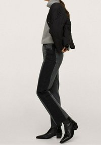 Veste matelassée noire portée sur un col roulé gris, associée à un jean gris foncé et des bottines noires. Le jean présente un panneau latéral contrastant.