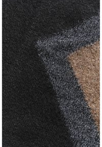 Coperta in lana con un motivo geometrico che presenta sezioni nere, grigie e marroni. Superficie testurizzata con spessori e fibre variabili.