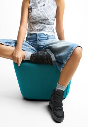 Črne teniske s visokim vrhom, opremljene s tremi ježki, iz semiša in mrežnega materiala, v kombinaciji s svetlo sivo rebrasto nogavicami in skrajšanimi jeans hlačami.