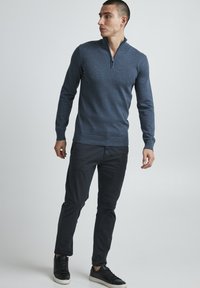 Maglione blu con zip al collo realizzato in tessuto lavorato a maglia; maniche lunghe; design aderente. Abbinato a pantaloni scuri e sneaker nere.