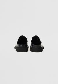 Zapatos deslizables de cuero negro con un acabado suave, abertura amplia y una suela de goma texturizada y resistente. Diseño minimalista sin adornos.