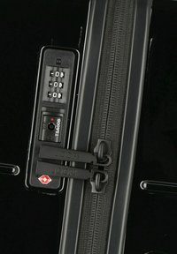 Black hard-shell suitcase zipper with combination lock, TSA-approved, featuring dual black zipper pulls and textured fabric along the zipper.