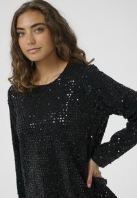Top a maniche lunghe nero ricoperto di paillettes; scollo rotondo, texture morbida, superficie lucida, forma aderente al corpo, vestibilità casual.