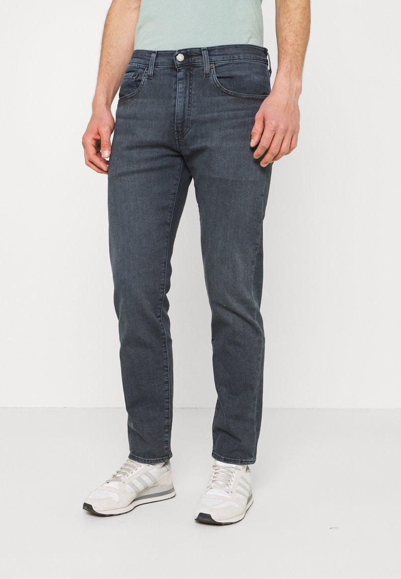 Mörkblå denimjeans med slim fit, femfickorsdesign och subtila bleknade detaljer. Kombinationen med vita sportskor.