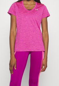 Mujer vistiendo una camiseta deportiva de manga corta de color rosa brillante con efecto jaspeado y leggings magenta sólidos con rayas rosas a los lados, de pie frente a un fondo blanco.