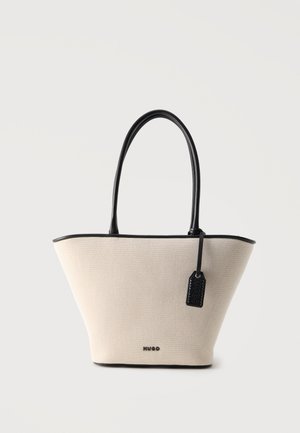 Borsa tote strutturata beige con manici in pelle nera, bordature e un'etichetta nera appesa con il nome del marchio su sfondo bianco.