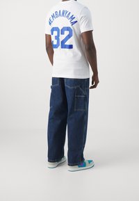 Biała koszulka z napisem „WEMBAINYAMA” i liczbą „32” w kolorze niebieskim. Dobranie do luźnych, ciemnoniebieskich spodni cargo z denimu. Buty sportowe z turkusowymi akcentami.