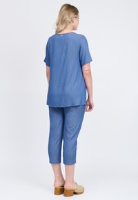 Maglietta in chambray blu con maniche corte e dettaglio dei bottoni sul retro, abbinata a pantaloni cropped coordinati. Tessuto liscio e vestibilità comoda.