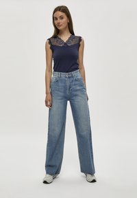 Top blu navy con dettagli in pizzo sul collo, abbinato a jeans a vita alta, larghi e di un leggero blu, e scarpe da ginnastica grigie. Outfit semplice e casual.